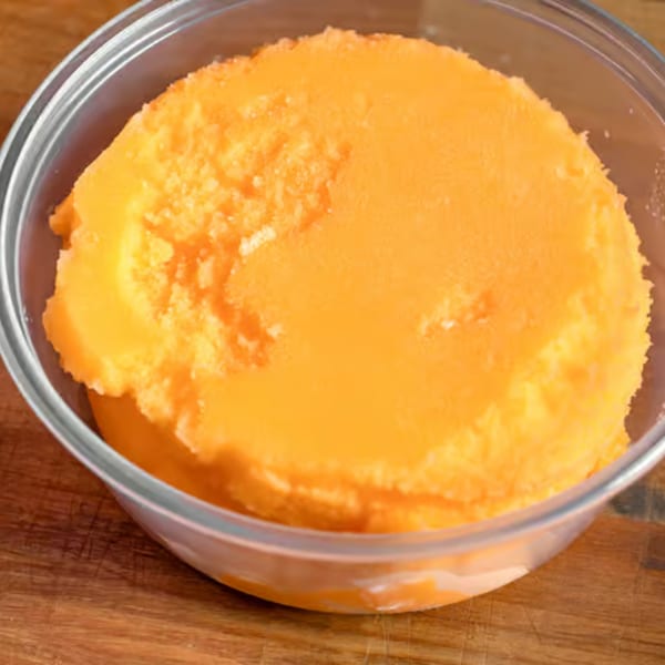 Bright orange sorbet or ice cream in a clear glass bowl on a wooden surface.