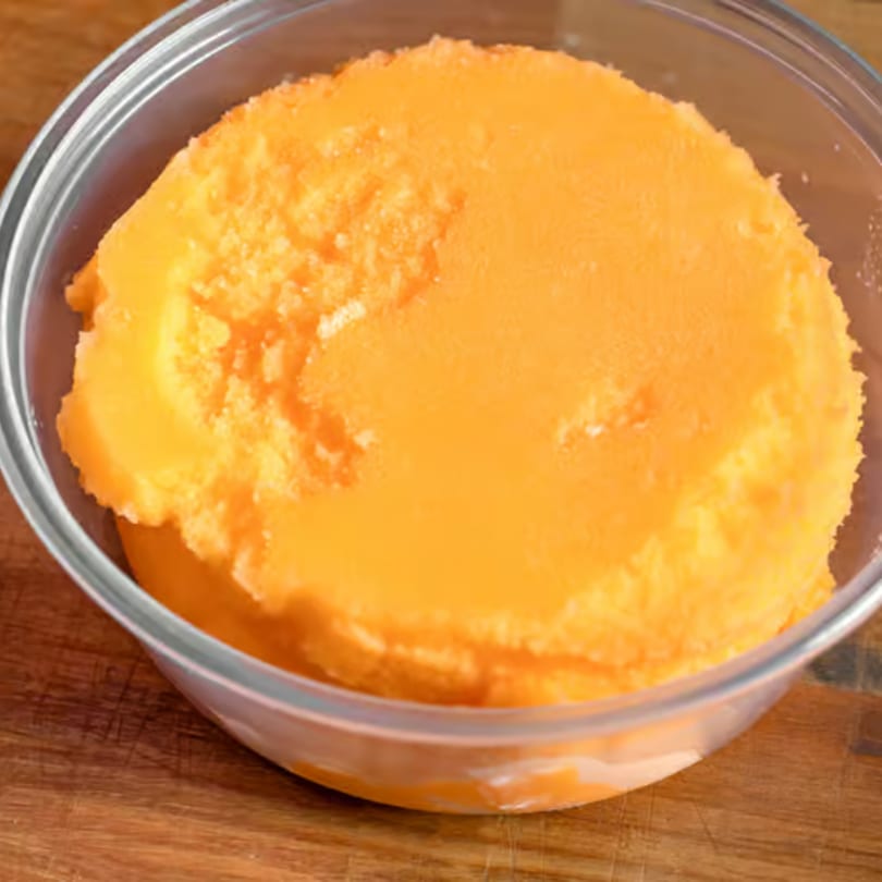 Bright orange sorbet or ice cream in a clear glass bowl on a wooden surface.