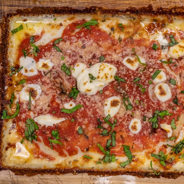 Close-up of a rectangular Detroit-style pizza with crispy crust, red sauce, melted cheese, and fresh basil.