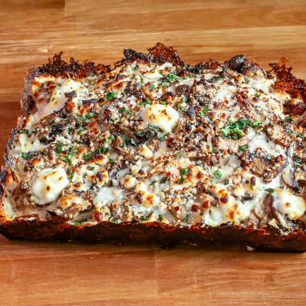 Close-up of a rectangular mushroom and cheese flatbread, garnished with fresh herbs, on a wooden surface.