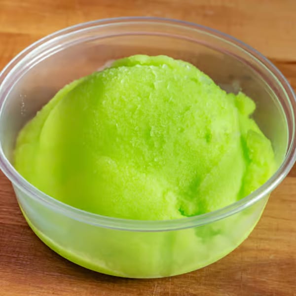 Bright green sorbet in a clear plastic cup, sitting on a wooden surface.