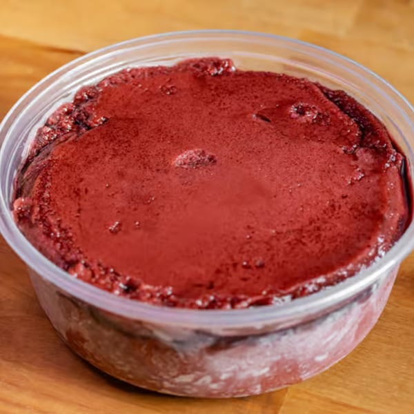 A clear plastic container filled with frozen, dark red açaí on a wooden surface.