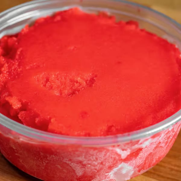 Close-up of vibrant red sorbet or granita in a clear glass bowl on a wooden surface.