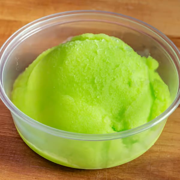 Bright green sorbet in a clear plastic cup, resting on a wooden surface.