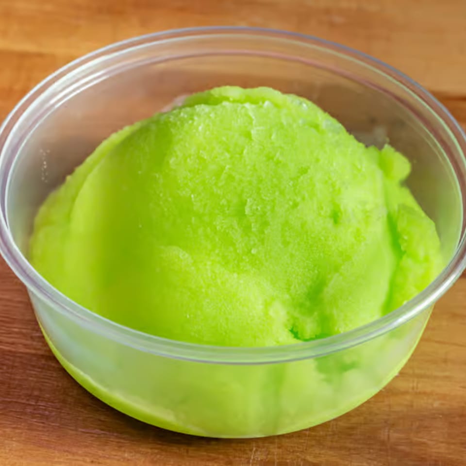 Bright green sorbet in a clear plastic cup, resting on a wooden surface.