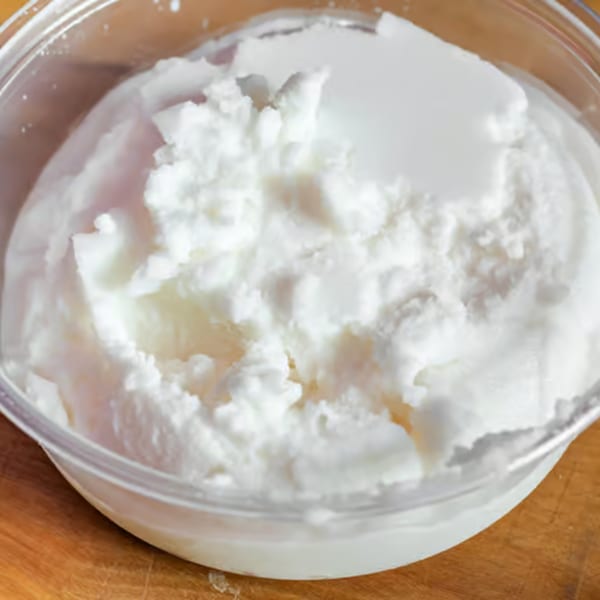A clear plastic container filled with fluffy white ricotta cheese on a wooden surface.