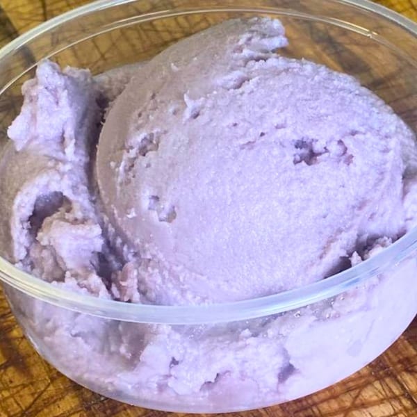 Close-up of purple ube ice cream in a clear plastic container on a wooden surface.
