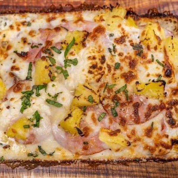 Close-up of a Hawaiian pizza with melted cheese, ham, pineapple, and green herbs.